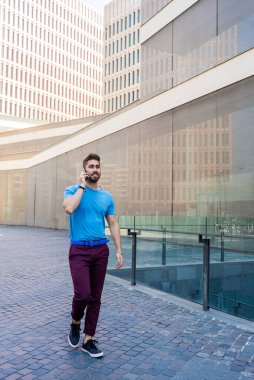 Modern businessman speaking by phone and smiling while standing outdoors