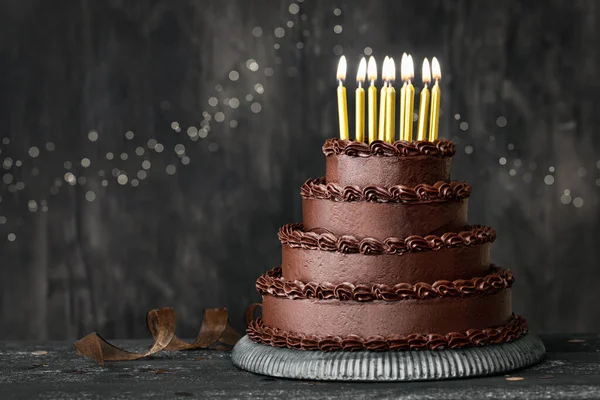 Tiered chocolate birthday cake decorated with chocolated frosting and gold birthday candles