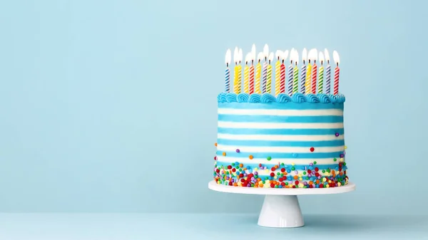 カラフルな誕生日キャンドルと青い背景にスプリンクル付きのストライプのバタークリームの誕生日ケーキ — ストック写真