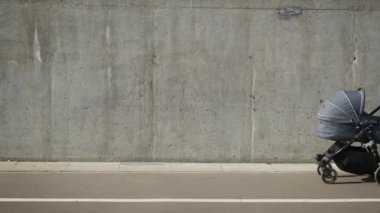 Elinde bebek arabası ve tuvalle şehirde gri beton duvarın yanında yürüyen bir anne. Bakıcı anne bebek arabasında yeni doğan bebeğe bakıyor. Sıfır atık ebeveynlik.