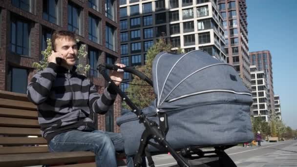 Knappe Jongeman Met Pasgeboren Kinderwagen Aan Het Praten Smartphone Terwijl — Stockvideo