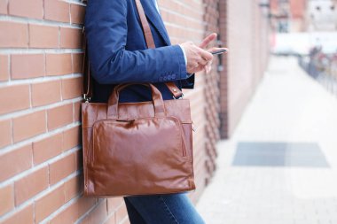 Şehirde tuğla duvarın yanında dururken akıllı telefon kullanan evrak çantalı sıradan bir iş adamı. Sokakta deri çantalı tanınmayan bir adam. Boşluğu kopyala.