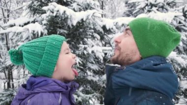 Father and son catching snowflakes by mouth outdoor. Child and dad on snowing winter weather. Positive emotion, kid expression, happy childhood.