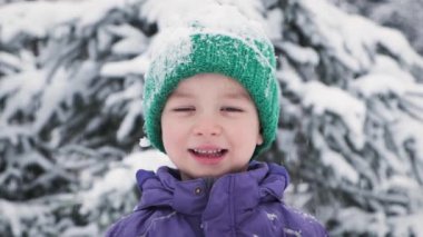 Dışarıda kar altında kameraya bakarak gülümseyen mutlu çocuk portresi. Mutlu 5 yıl kışın çocuk sevinci. Pozitif ve mutluluk kavramı.