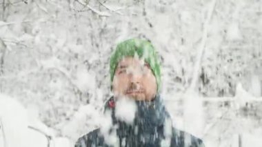 Winter portrait of handsome smiling bearded man looking at camera standing under snow covered trees outdoor. Headshot happy guy joy emotion in snowfall. Positive concept, snowing weather.