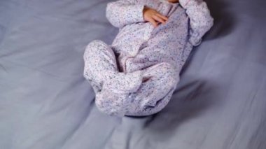 Cute legs of newborn baby in a purple lavender bodysuit lying on lilac sheet and moving legs. Baby foot. Very peri color of the year 2022 concept.