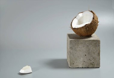 Creative conceptual still life with open coconut balance on concrete cube stand podium on gray background, with copy spacel. Minimal composition.