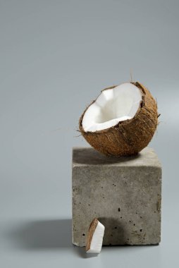 Creative conceptual still life with open coconut balance on concrete cube stand podium on gray background, vertical. Minimal composition.