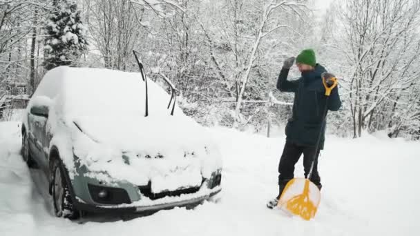 豪雪の後 慎重に雪の近くに立ってシャベルを持つ男は車を覆った 悪天候 自然災害 吹雪のために裏庭を掃除する人 — ストック動画
