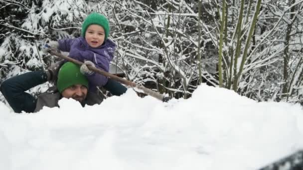 可爱的小男孩坐在父亲的肩上 大雪过后用刷子把雪从雪地覆盖的车顶上移开 — 图库视频影像