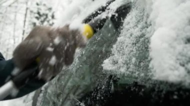 Close-up person removing ice snow and frozen hoarfrost from car window with scrap. Cold winter weather, natural disaster. Man cleaning scraping his car after snowstorm. Slow motion.