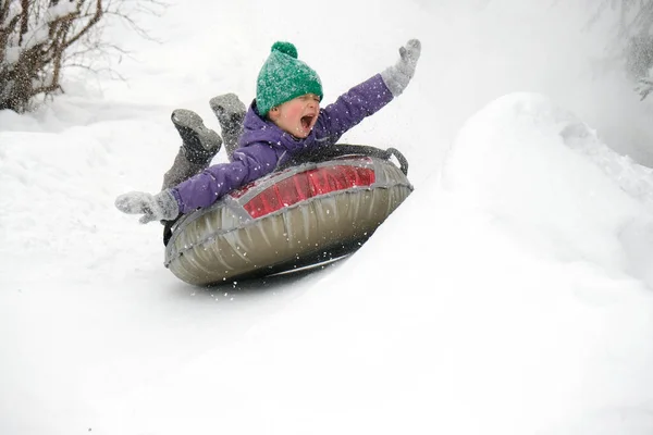 可爱的小男孩骑在雪地上 手举起来 小孩滑行滑向山下 冬季户外活动 图库照片