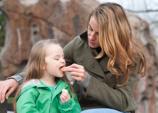 Little girl biting an apple from her mother's hands — Stock Photo, Image