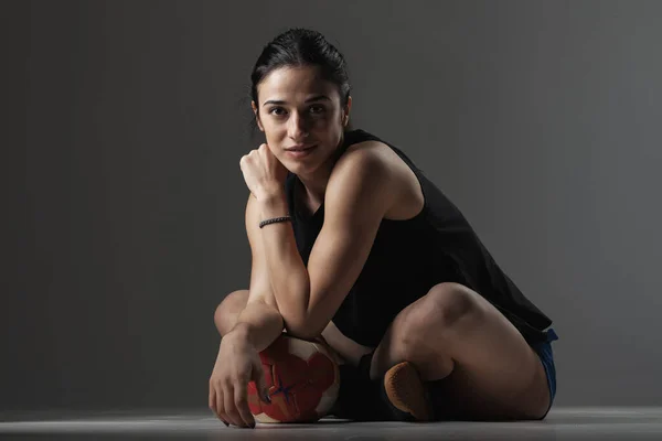 Handball player sitting on the ground. Girl posing with ball and making face expressions.