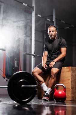Ağırlık kaldırma ekipmanlarıyla poz veren kaslı bir sporcu. Duman arkaplanı.