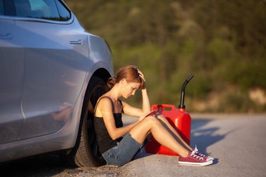 Üzgün kız yerde, kırmızı gaz tüplü elektrikli arabanın yanında oturuyor. Telefon bekletiliyor. 