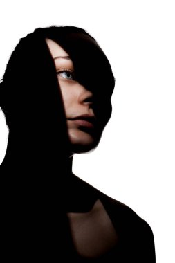 Şirin bir kızın moda stüdyo portresi. Yüzünde sert gölgeler olan genç ve güzel bir kadının silueti. beyaz arka plana karşı.