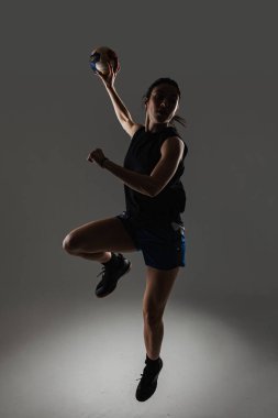 Hentbolcu gri arka planda poz veriyor. Topla zıplayan kız.