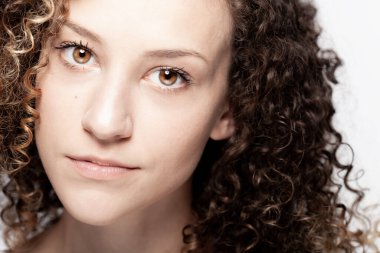 Uzun kıvırcık saçlı güzel esmer kız. Yakın çekim stüdyo portresi. Ciddi yüz ifadesi.