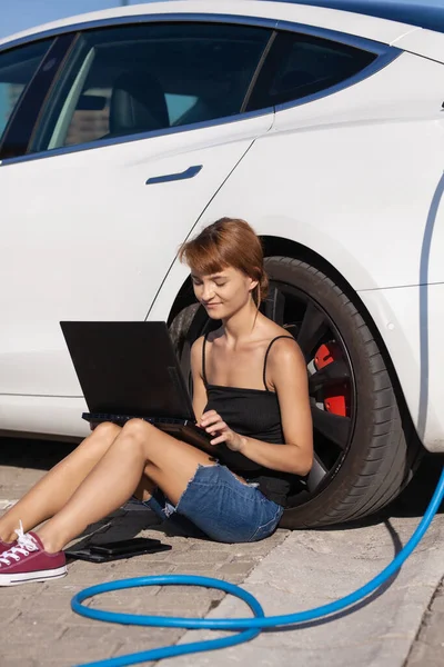 Lány Földön Vár Miközben Elektromos Autója Töltődik Laptopon Dolgozni — Stock Fotó