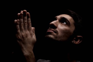 Karanlık odada dua eden kendinden emin bir gencin vesikalığı. Yukarıdan aydınlat ve yukarı bak..