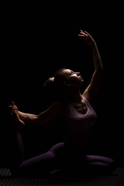 Stüdyoda yoga yapan formda bir kız. Yarı siluet yan aydınlatma fitness modeli