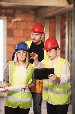 Yelekli ve başlıklı mühendislerden oluşan bir ekip bir tabletin içinde, inşaat alanında.