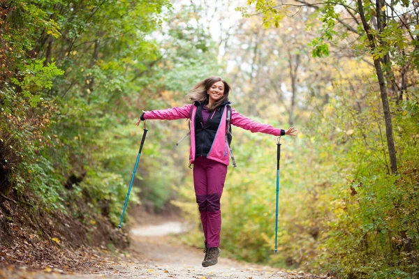 远足的女孩在山上的小径上跳着 背包客 带着远足杆和粉色夹克在森林里 户外运动快乐 — 图库照片