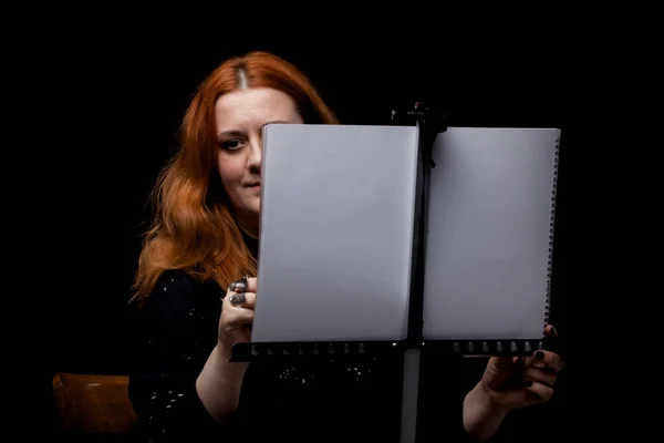 Red hair woman painting. Portrait of an artist against black background.
