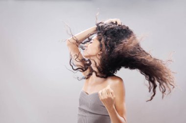 Havada uzun kıvırcık saçlı güzel esmer kız, stüdyo portresi. Ciddi yüz ifadesi.