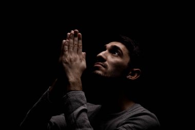 Karanlık odada dua eden kendinden emin bir gencin vesikalığı. Yukarıdan aydınlat ve yukarı bak..