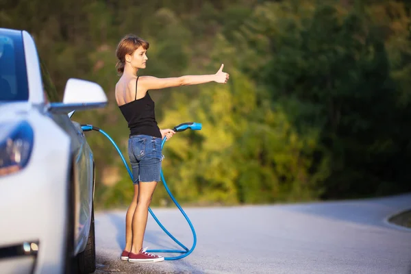 Κορίτσι Στέκεται Δίπλα Στο Ηλεκτρικό Αυτοκίνητο Κρατώντας Ένα Καλώδιο Φόρτισης — Φωτογραφία Αρχείου