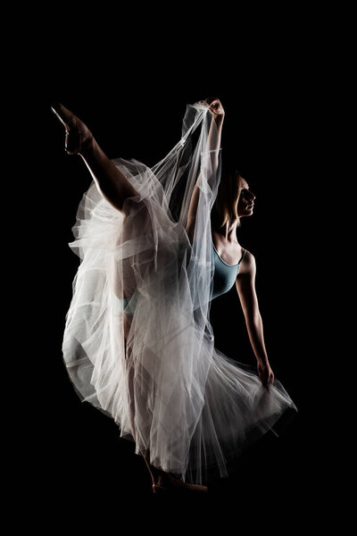 Ballerina with a white dress and black top posing on black background
