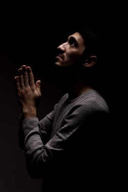 Karanlık odada dua eden kendinden emin bir gencin vesikalığı. Yukarıdan aydınlat ve yukarı bak..