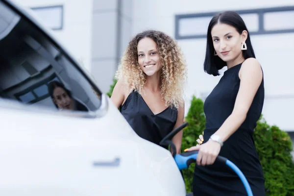 Két Gyönyörű Üzletasszony Fekete Outfutetben Pózol Egy Elektromos Autó Mellett — Stock Fotó