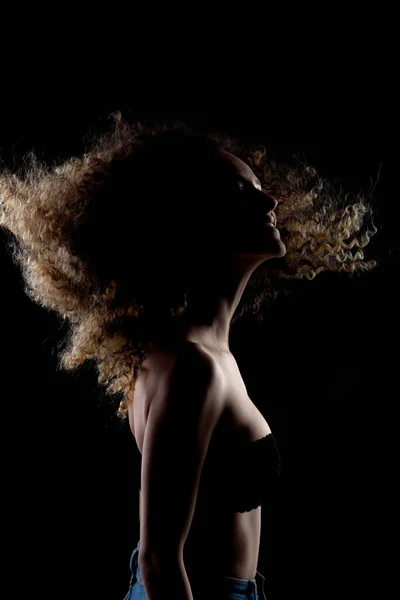 サイドは空気中の長い巻き毛のブルネットの女の子を点灯しました シルエット スタジオ ポートレート暗い背景 — ストック写真