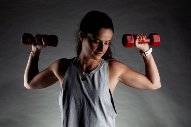 Fitness kızı poz veriyor ve ağırlık kaldırıyor. Olumlu gülümseme ifadesi.