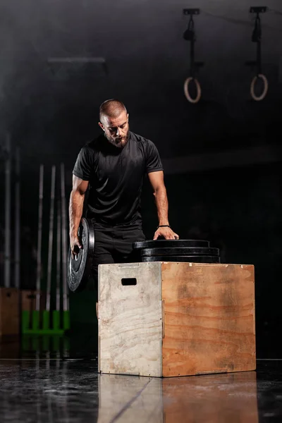 Muscular athlete posing with weightlifting equipment. Smoke background.