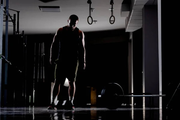 Silhouette of a muscular athlete with weights. Standing next to heavy barbell.