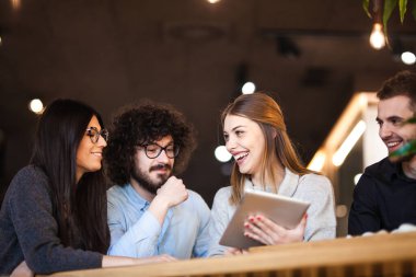 Bir kafede oturmuş tablete bakarak sohbet eden dört arkadaş. Pozitif yüz ifadeleri.