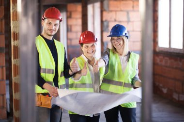 Yelekli ve kasklı mühendislerden oluşan bir ekip bir inşaat sahasında başparmaklarını gösteriyorlar.