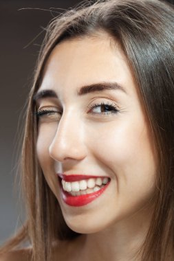 Güzel esmer kız stüdyo resmi. Göz kırpan ve gülümseyen yüz ifadesi.