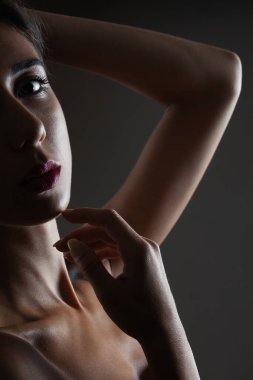 Güzel esmer kız stüdyo resmi. Koyu arkaplanda yarım siluet var. Ciddi yüz ifadesi.