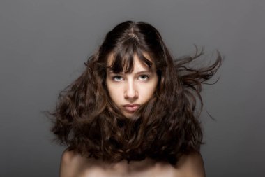 Gri arka planda güzel bir genç kız stüdyo resmi. Kameraya bakıyorum. Rüzgarlı saçlar.