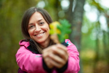Pembe elbiseli kız elinde iki sonbahar yaprağı tutuyor. Dağlarda sonbahar sezonu.