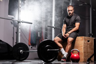 Ağırlık kaldırma ekipmanlarıyla poz veren kaslı bir sporcu. Duman arkaplanı.