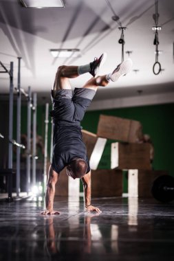 Ayakta duran ve baş aşağı yürüyen kaslı bir sporcu.