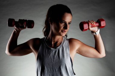 Fitness kızı poz veriyor ve ağırlık kaldırıyor. Olumlu gülümseme ifadesi.