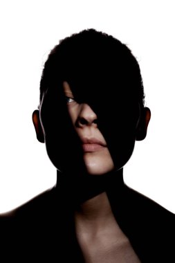 Şirin bir kızın moda stüdyo portresi. Yüzünde sert gölgeler olan genç ve güzel bir kadının silueti. beyaz arka plana karşı.