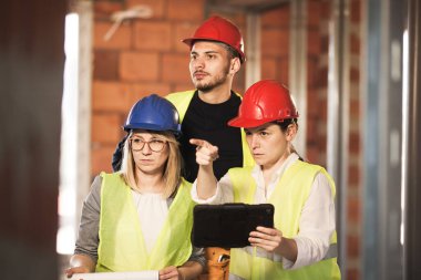 Yelekli ve başlıklı mühendislerden oluşan bir ekip bir tabletin içinde, inşaat alanında.